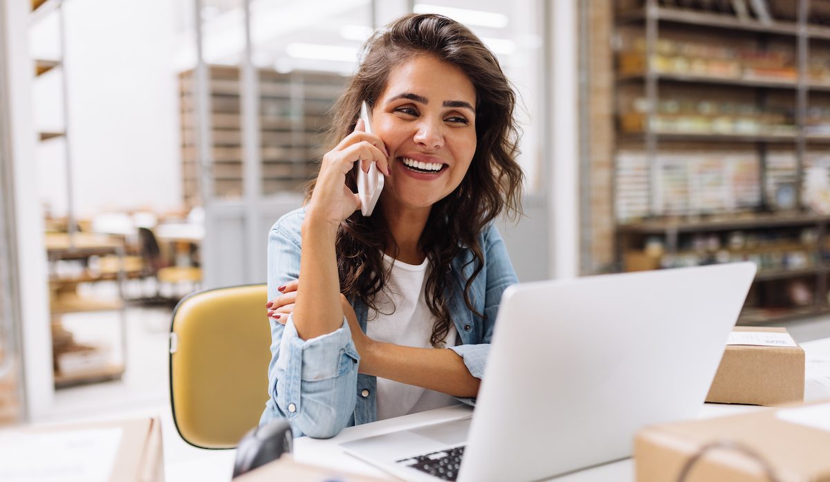 Happy young businesswoman speaking on the phone in a warehouse