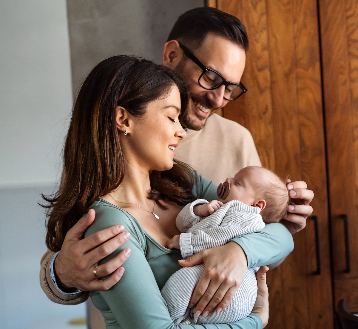 Portrait of young happy man and woman holding newborn cute babe dressed in white unisex clothing.